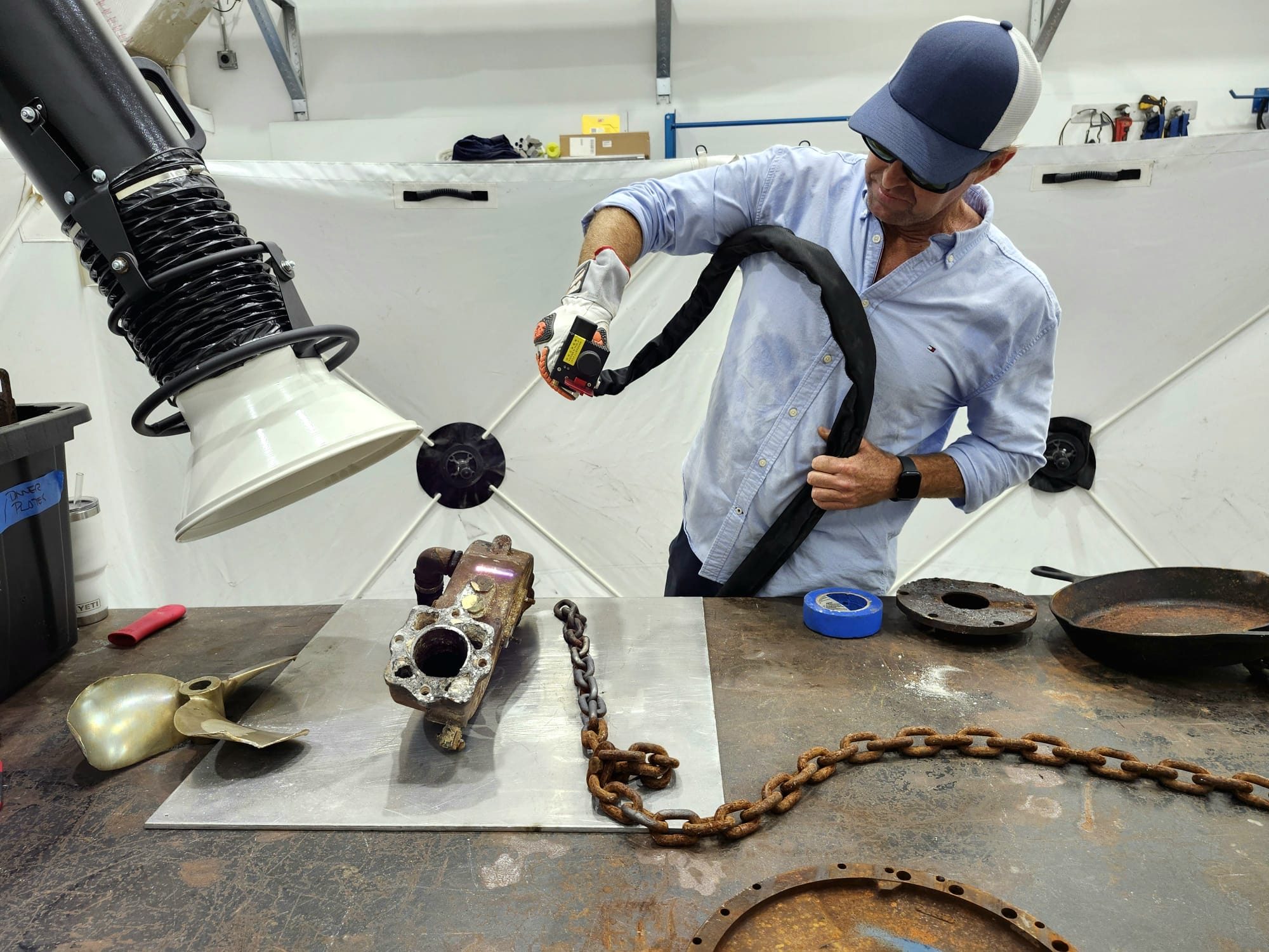 Handheld laser cleaning a corroded part at a workbench, with fume extraction